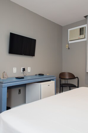 A hotel room with a bed, a desk with a computer, a chair, a television, and an air conditioning unit. - Master Express Alberto Bins (Porto Alegre)