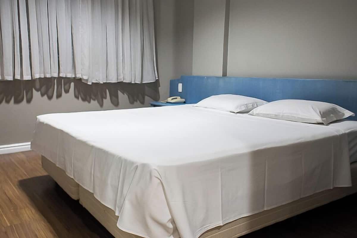 A neatly made bed with white linens, a blue headboard, and a bedside table with a phone.