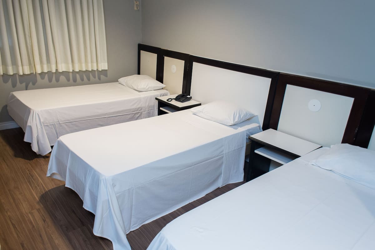 A hotel room with two single beds, a nightstand with a phone, and a window with curtains.