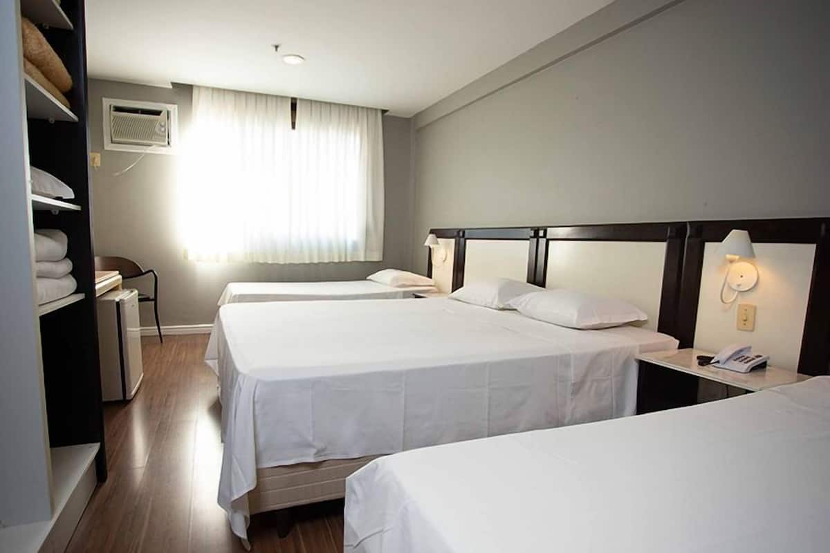 A hotel room with two beds, a wardrobe, a desk with a lamp, and an air conditioning unit.