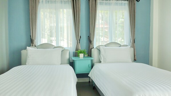 A twin room with two beds, a small table with a plant, and curtains on the windows. - Kata Bai D Inn (Karon)