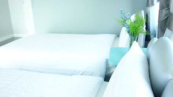 A modern hotel room with two beds, a teal accent pillow, and a vase with flowers.