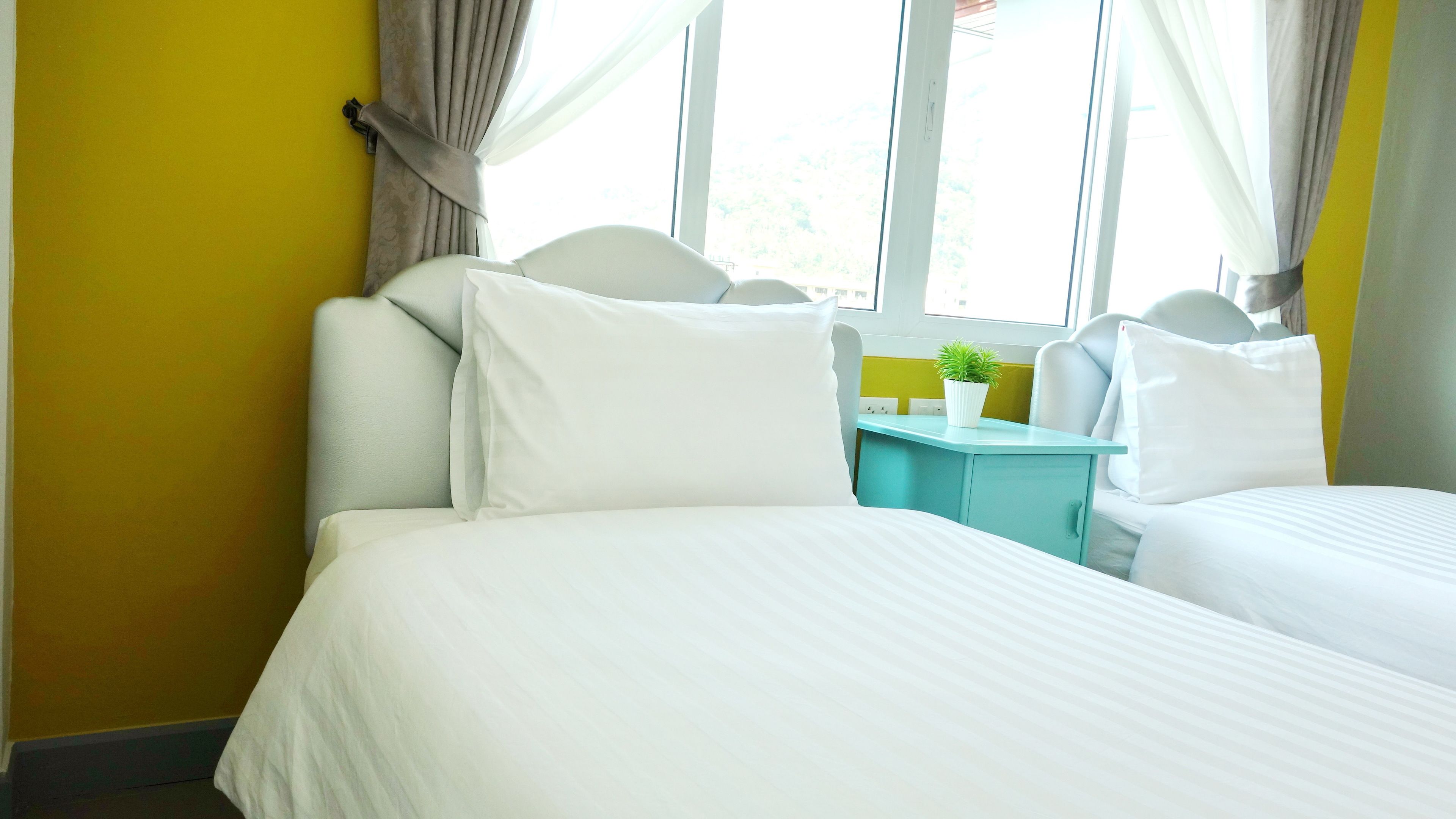 A hotel room with two beds, a small table with a plant, and a window with curtains.