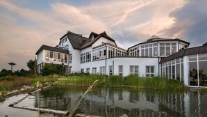 A large, modern house with multiple windows and a large glass door, situated next to a body of water. - Balmer See - Hotel · Golf · Spa (Benz)