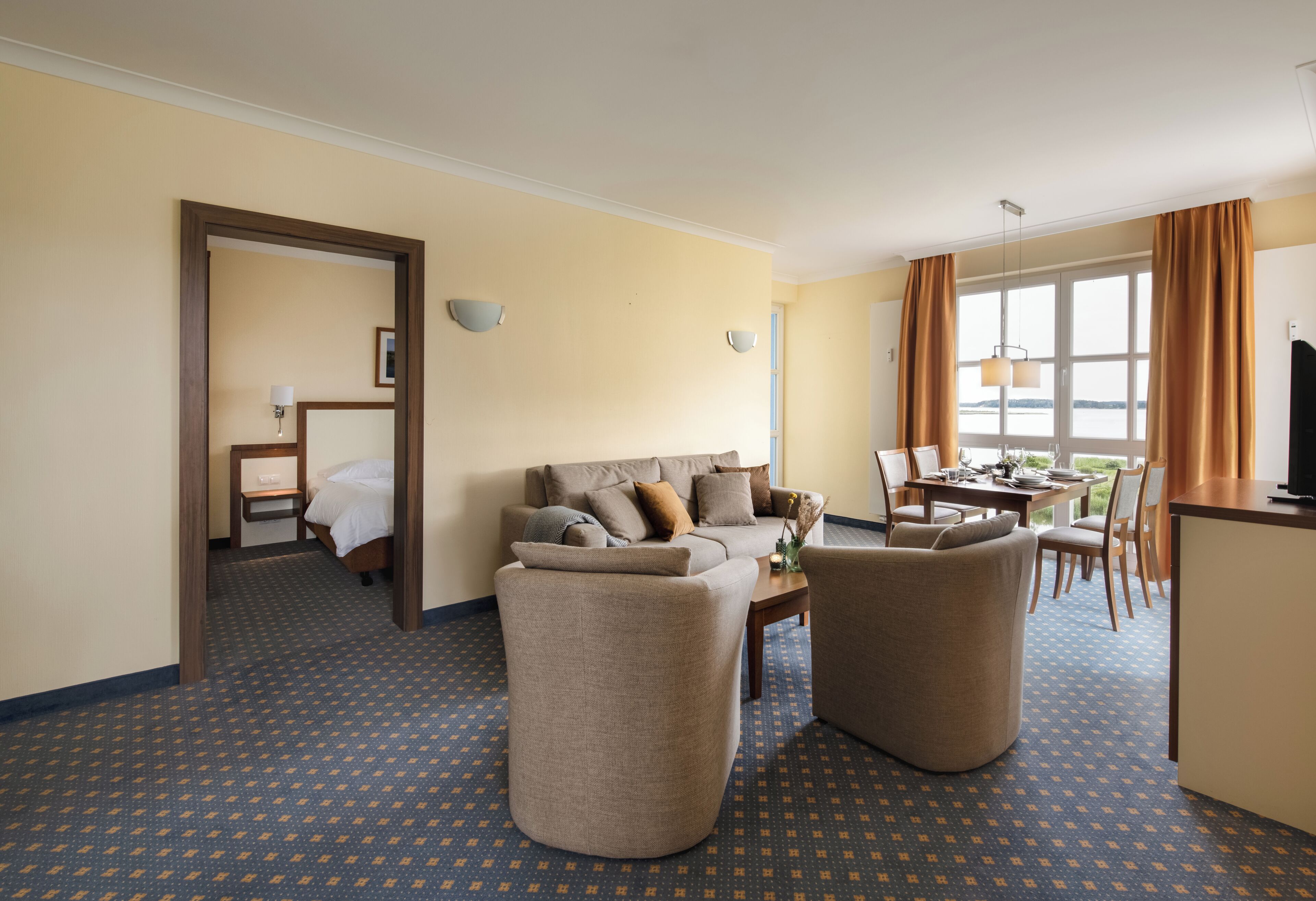 A hotel room with a sofa, armchairs, a dining table, and a TV.