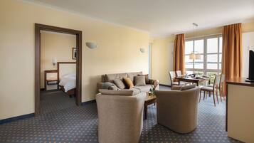 A hotel room with a sofa, armchairs, a dining table, and a TV.