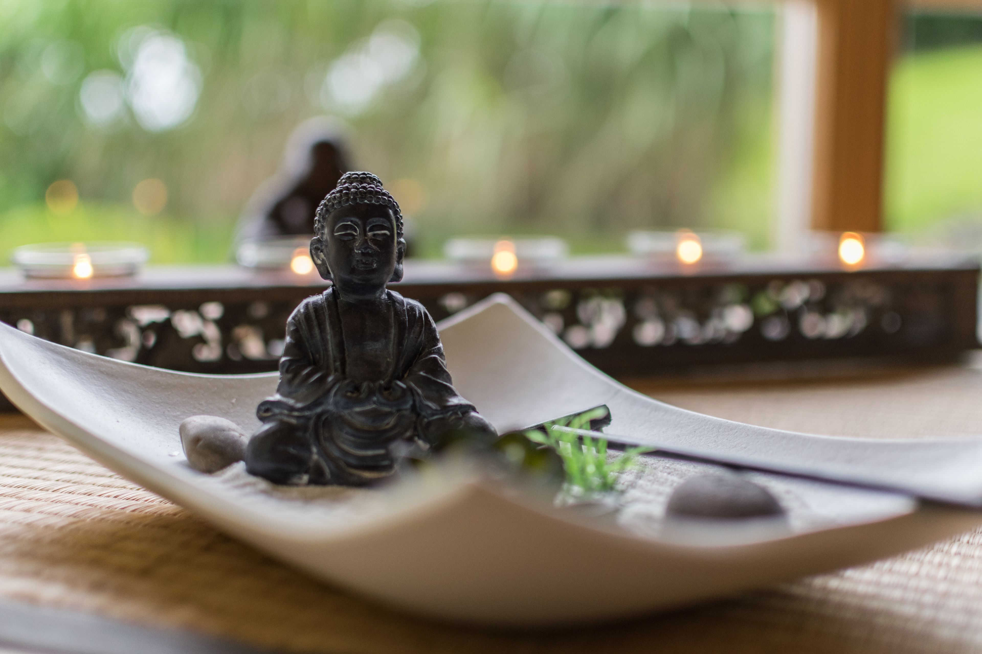 A Buddha statue on a white tray with a candle holder in the background.