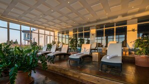 A sunlit indoor seating area with cushioned chairs, potted plants, and large windows offering views of the surrounding landscape. - Balmer See - Hotel · Golf · Spa (Benz)