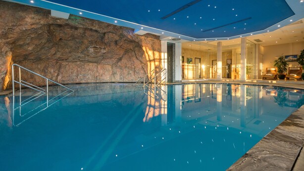 An indoor swimming pool with a rocky wall, clear water, and a well-lit interior. - Balmer See - Hotel · Golf · Spa (Benz)