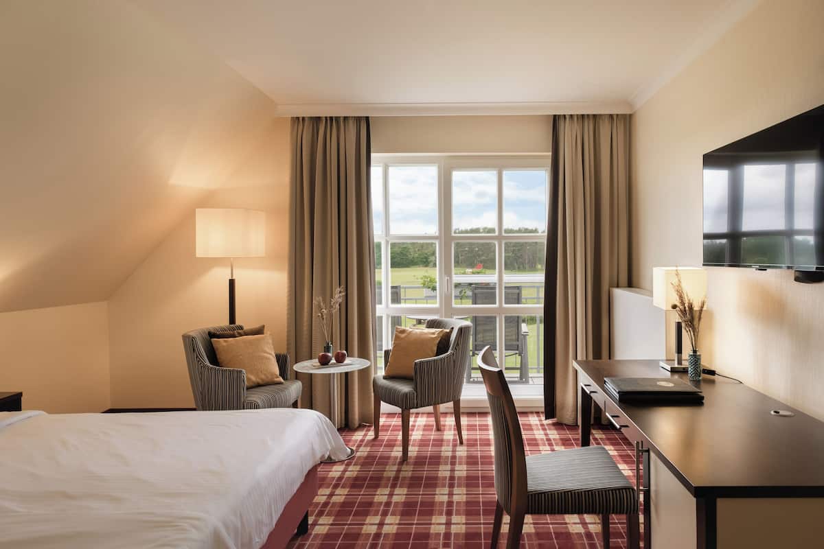 A hotel room with a bed, a desk, a chair, a small table, and a TV.