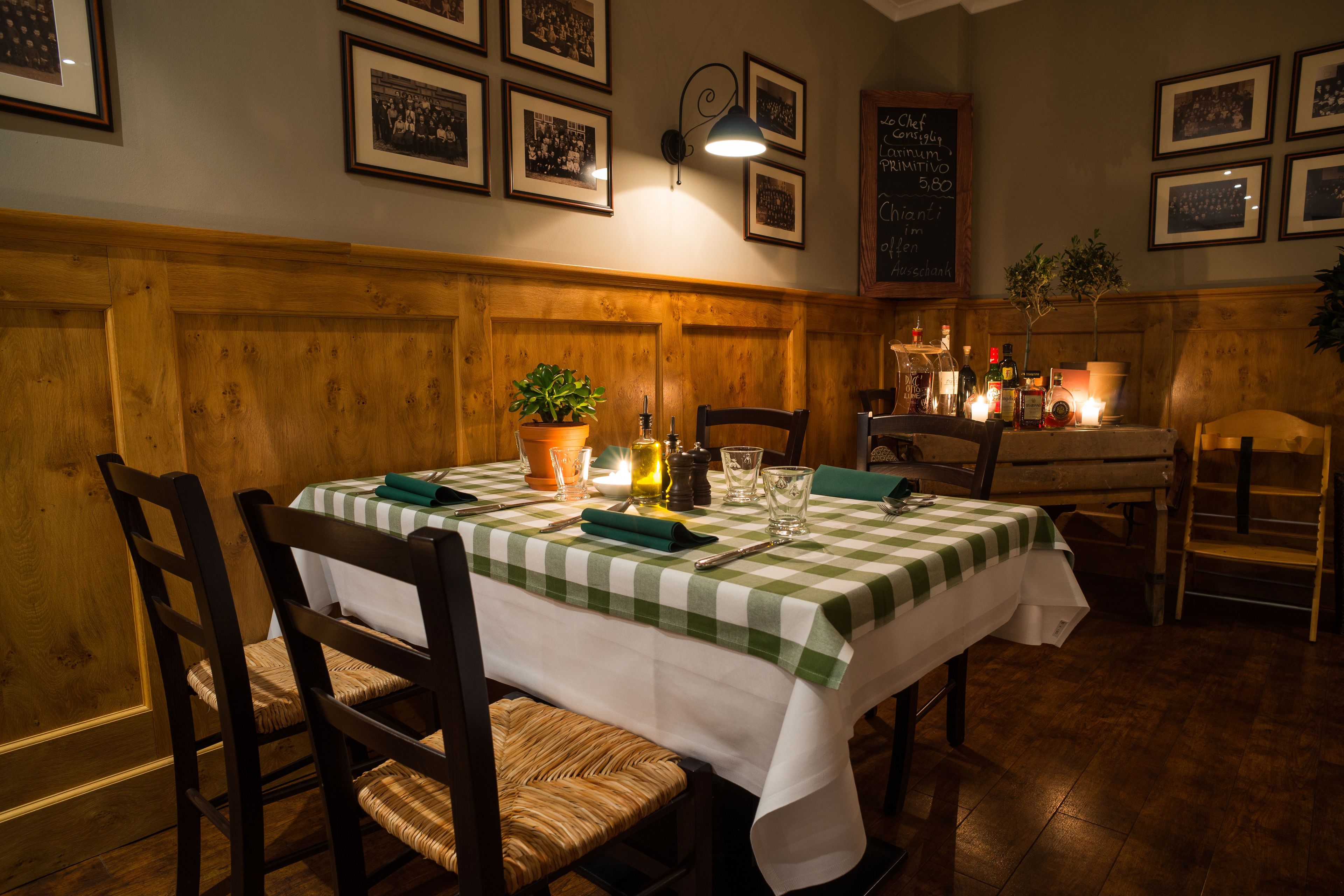 A dining area with a checkered tablecloth, wooden chairs, a potted plant, and a lit candle.