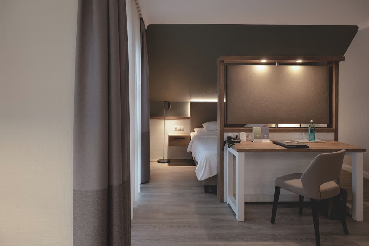 A modern hotel room with a bed, a desk, a chair, and a large mirror.