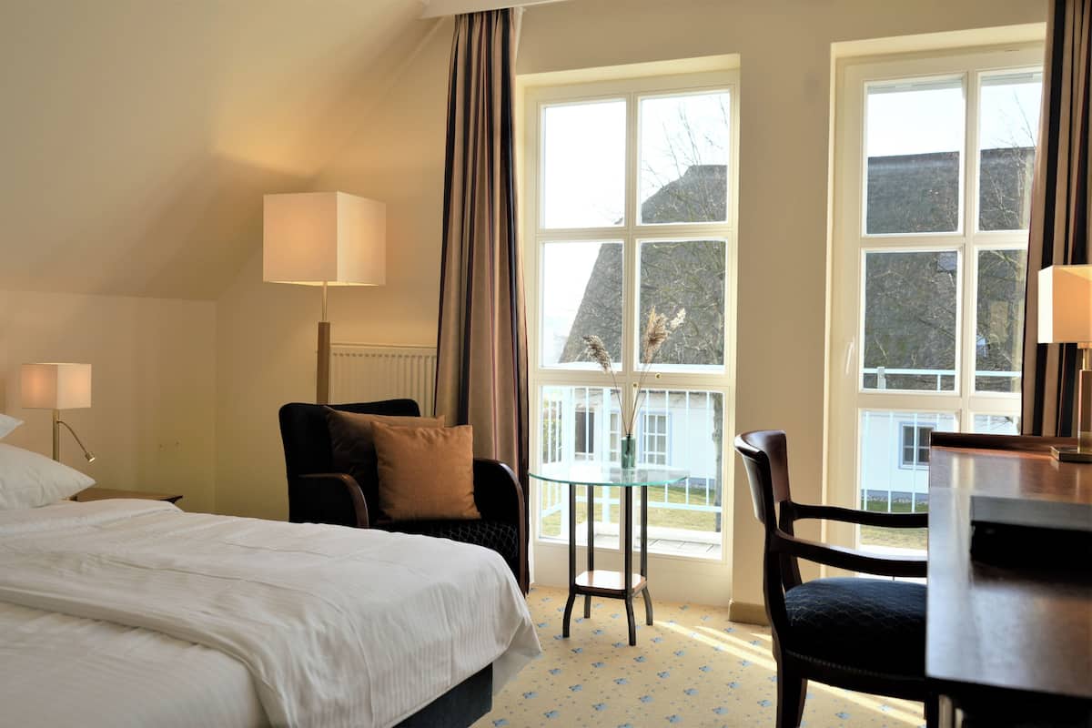 A hotel room with a bed, two chairs, a small table, and large windows offering a view of the outside.