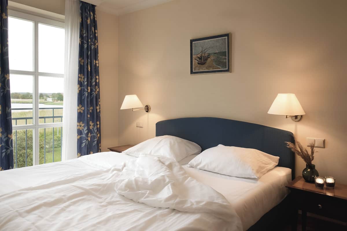 A hotel room with a large bed, two bedside lamps, a framed picture on the wall, and a window with curtains.