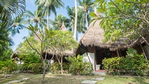 Un complex turístic tropical amb cabanyes de palla, vegetació exuberància i un cel blau clar.
