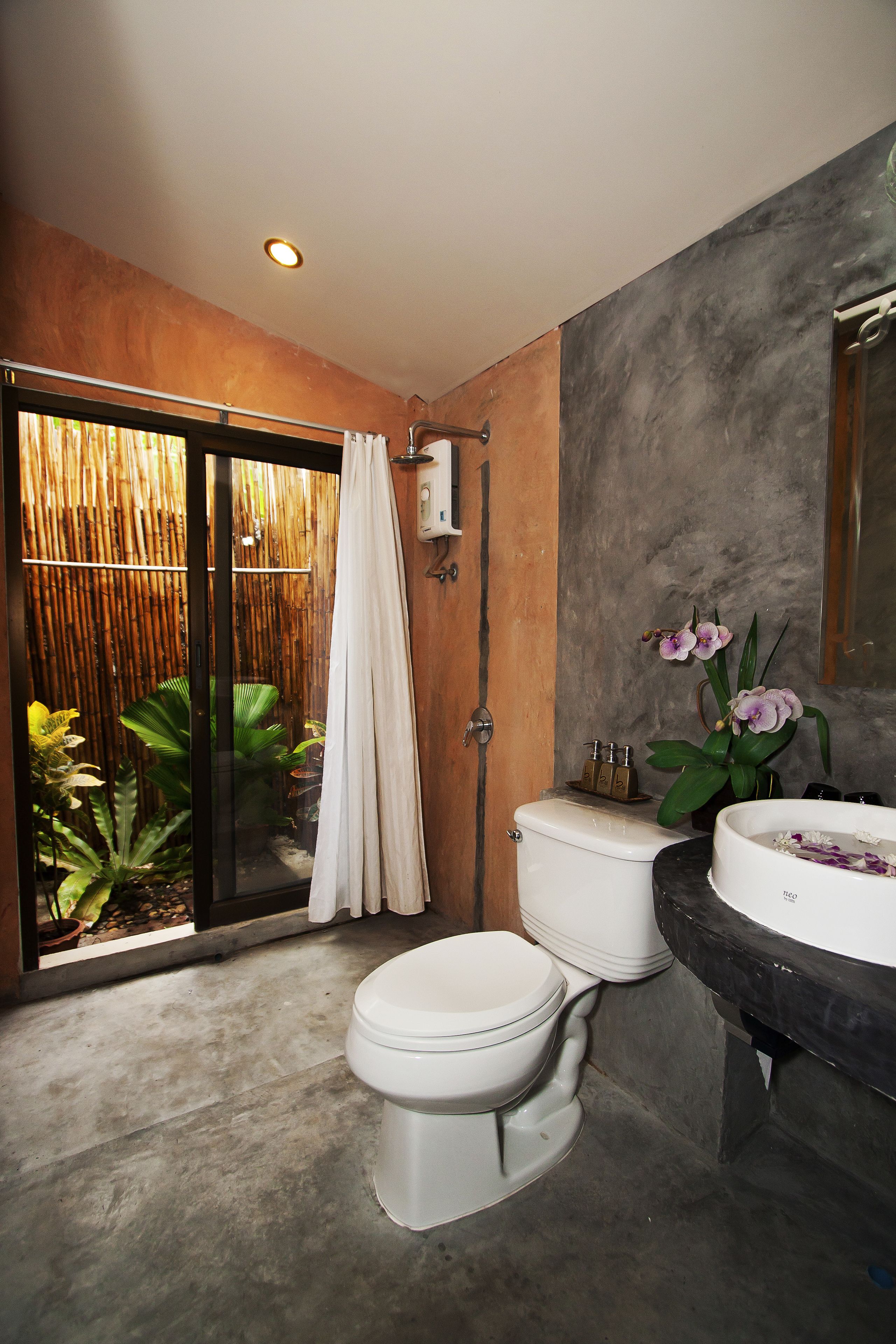 A bathroom with a toilet, bidet, and sink. There is a bamboo screen and a plant near the toilet.