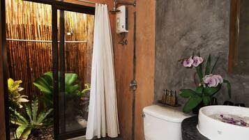 A bathroom with a toilet, bidet, and sink. There is a bamboo screen and a plant near the toilet.