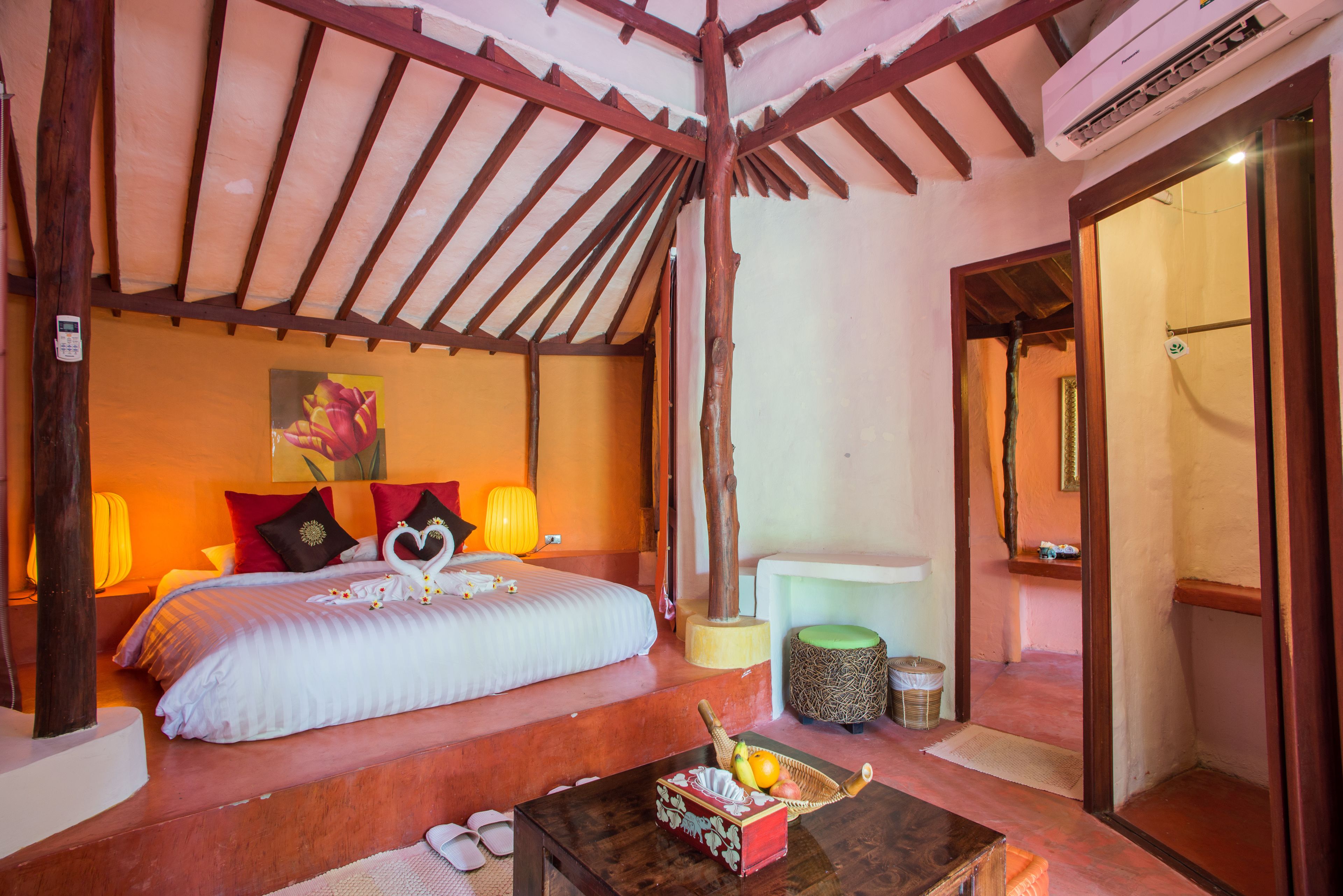 A bedroom with a wooden ceiling, a bed with white bedding, two bedside lamps, and a fruit basket on a wooden table.