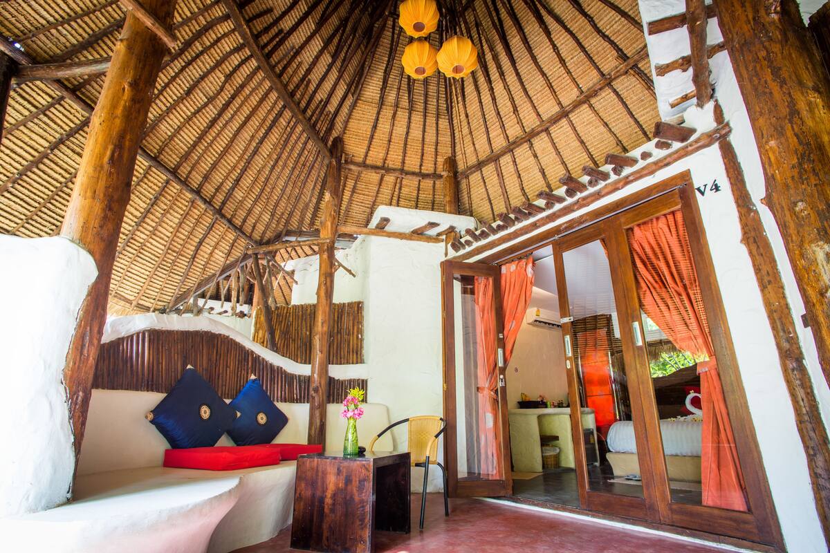 A room with a thatched roof, a sofa with cushions, a small table, and a chair.