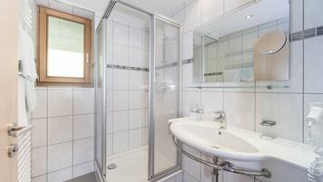 A modern bathroom with a glass shower enclosure, a white sink with a mirror above, and a wooden-framed window.
