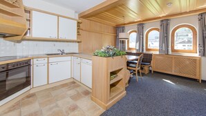 Una cucina compatta con piano cottura, lavello e pensili in legno. C'è un'area pranzo con tavolo e sedie, e una finestra con tende.