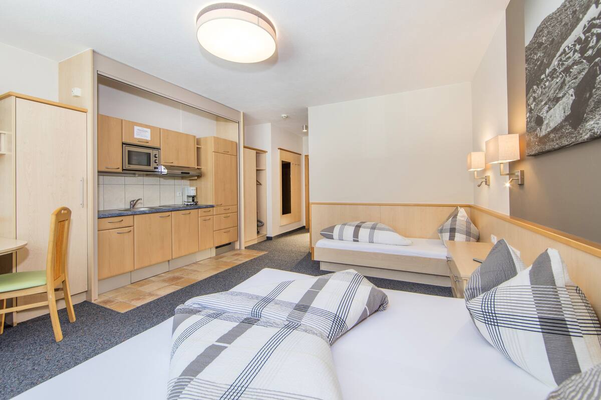 A compact hotel room with a kitchenette, a bed with striped bedding, a small table, and a chair.