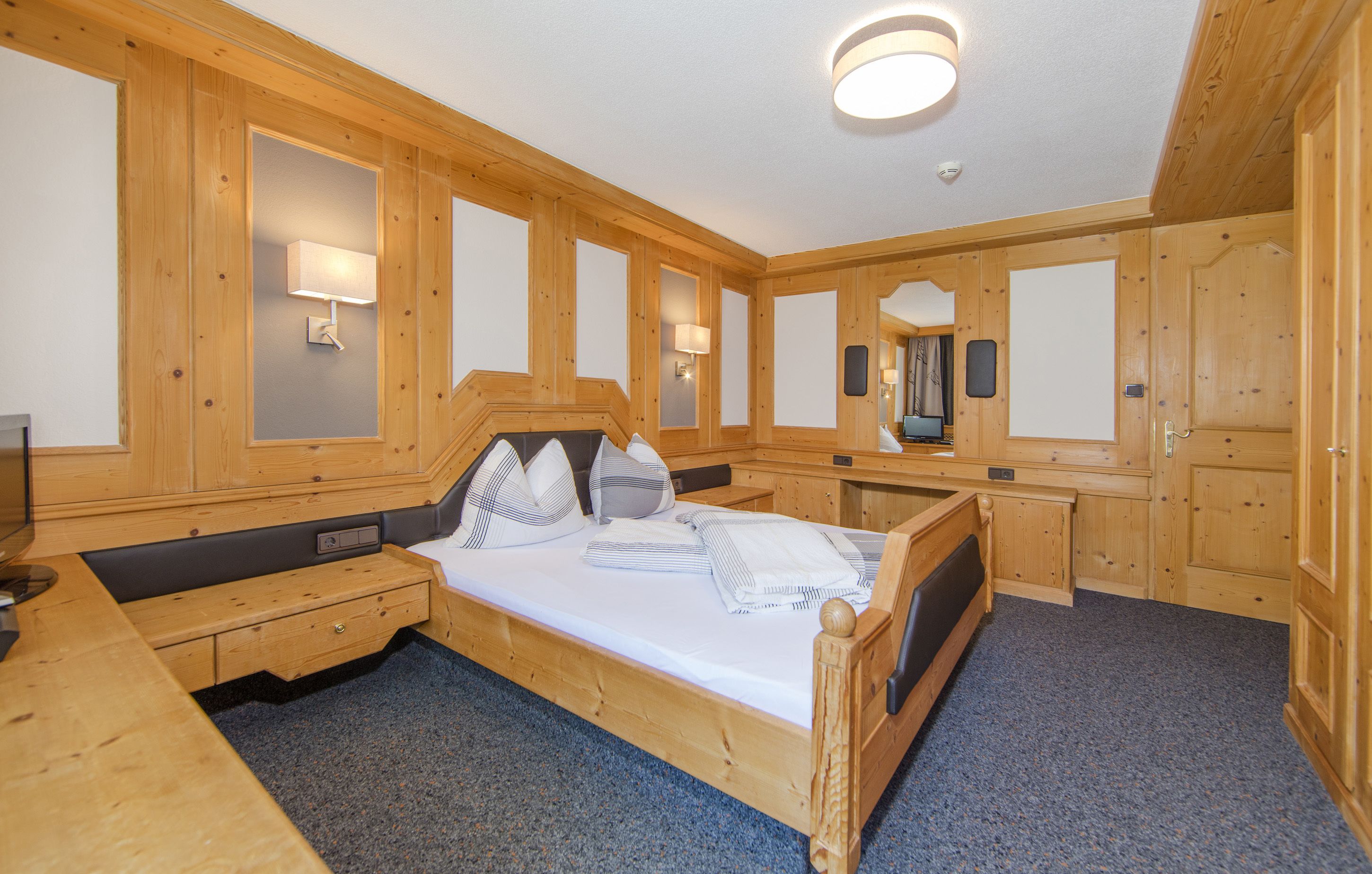 A wooden-paneled room with a bed, bedside tables, and a mirror.
