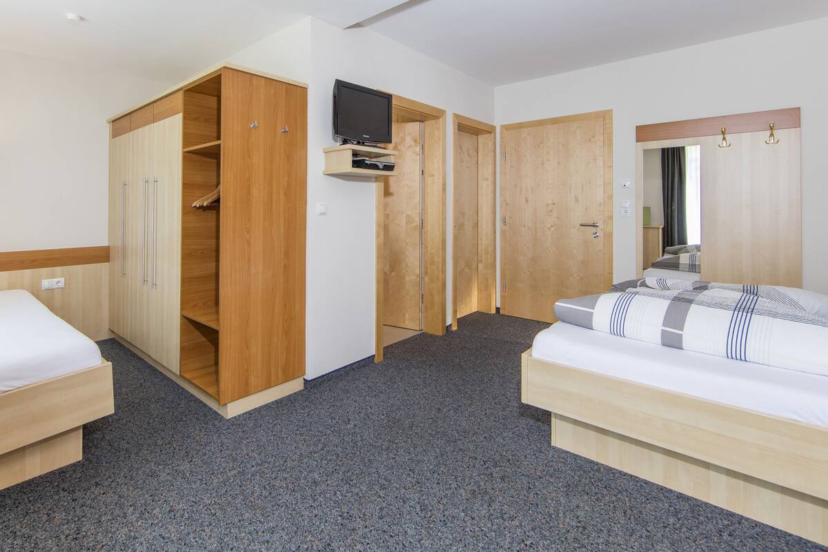 A hotel room with two beds, a TV, wooden wardrobes, and a carpeted floor.