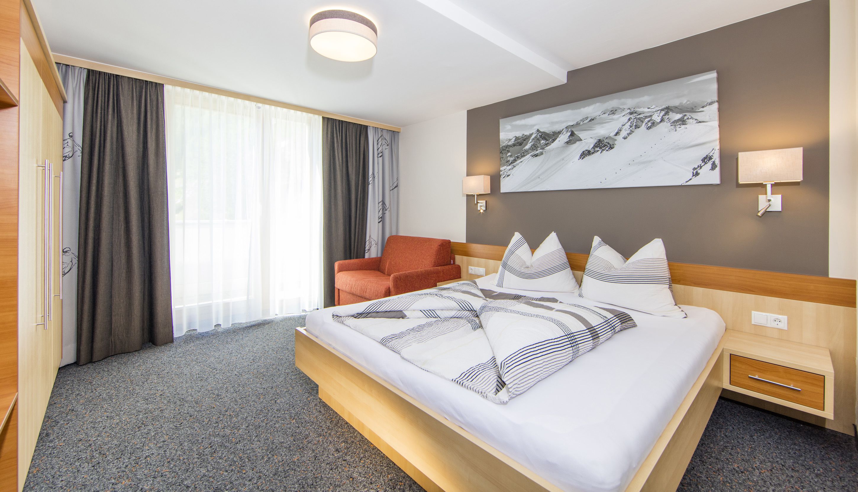 Een hotelkamer met een groot bed, een stoel, een schilderij aan de muur en een raam met gordijnen.