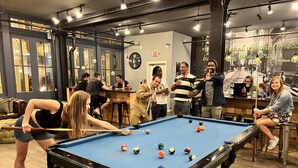 Een pooltafel in een ruimte met een bar, houten vloeren en een klok aan de muur.