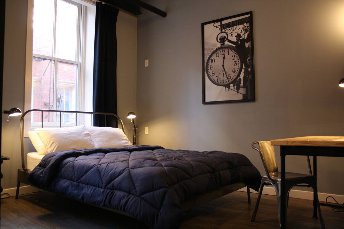 A bedroom with a bed, a desk, and a wall clock.