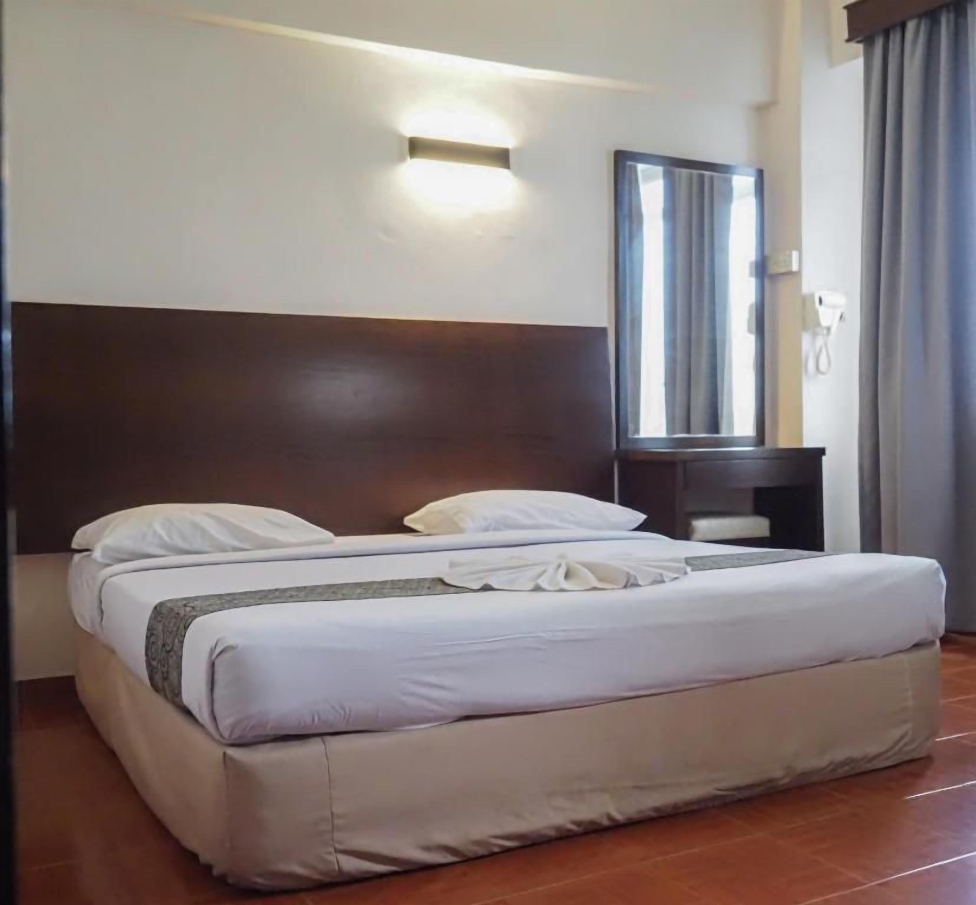 A hotel room with a large bed, a bedside table, a mirror, and a wall-mounted light fixture.