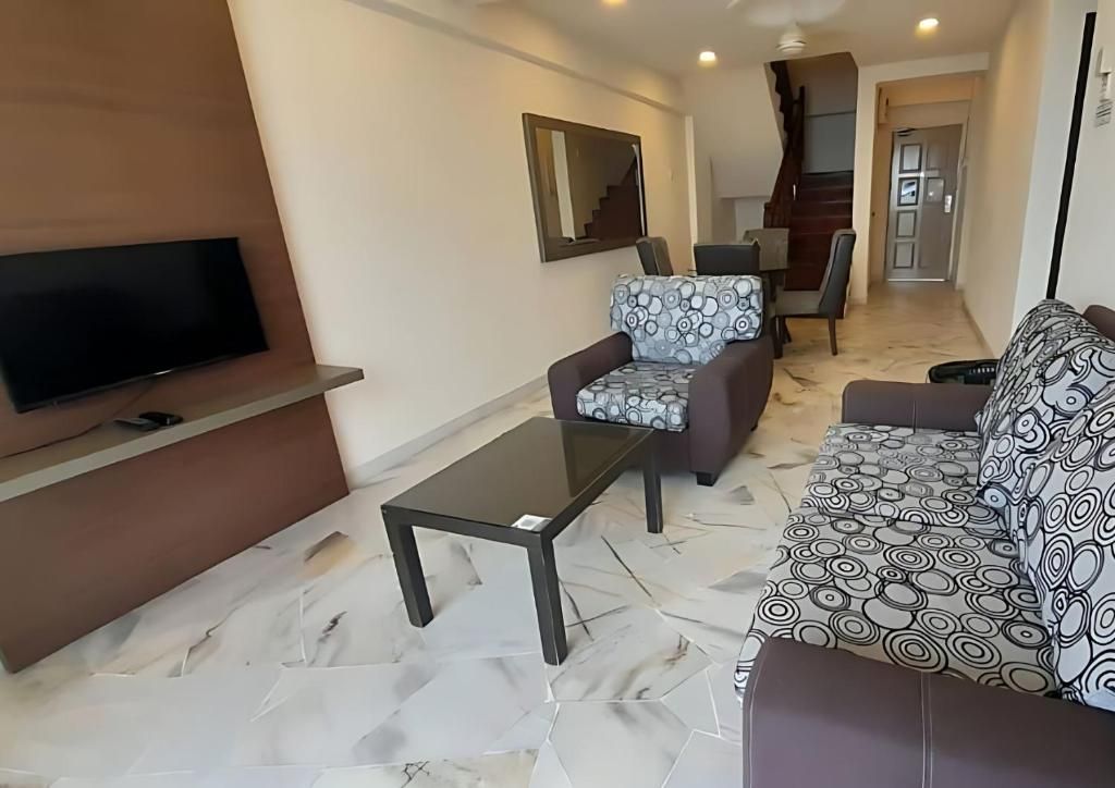 A living room with a flat-screen TV, a sofa, a patterned armchair, and a coffee table.