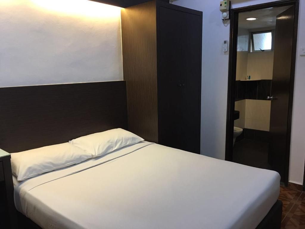 A single bed with white bedding, a wooden headboard, and a wall-mounted light.