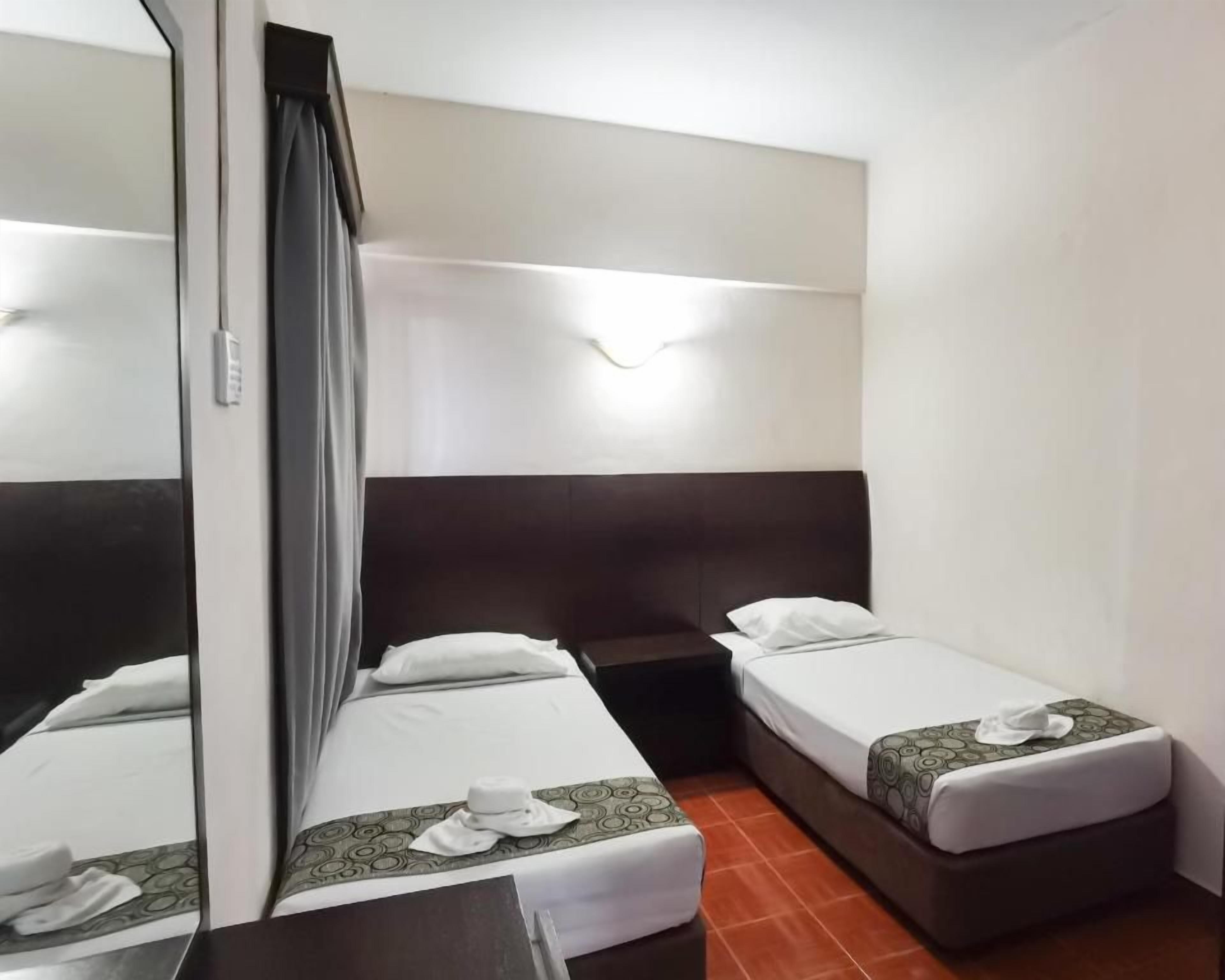 A hotel room with two single beds, a large mirror, and a bedside table.