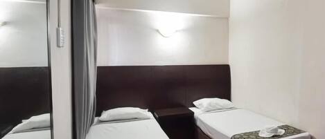 A hotel room with two single beds, a large mirror, and a bedside table.