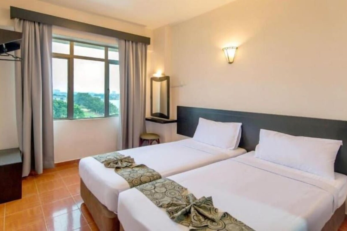 A hotel room with two beds, a window with curtains, a wall-mounted light, and a small table with a mirror.
