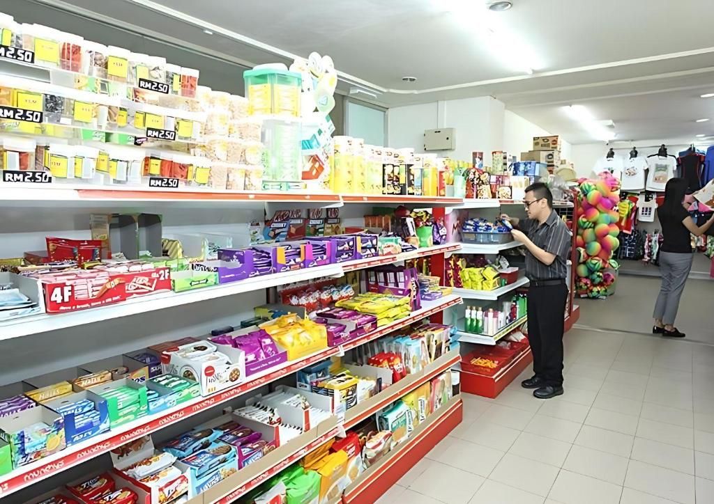 Un pasillo de supermercado con diversos productos envasados en estantes, una persona observando los artículos y otra al fondo.