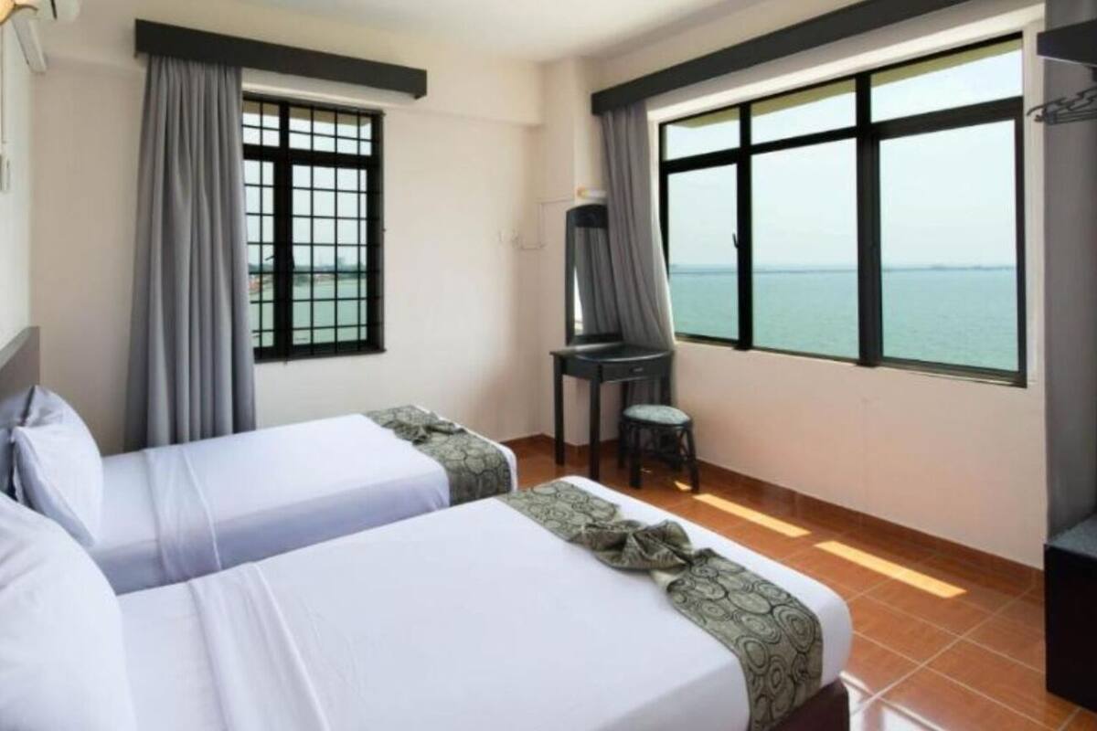 A hotel room with two beds, a treadmill, a chair, and large windows with a view of the sea.
