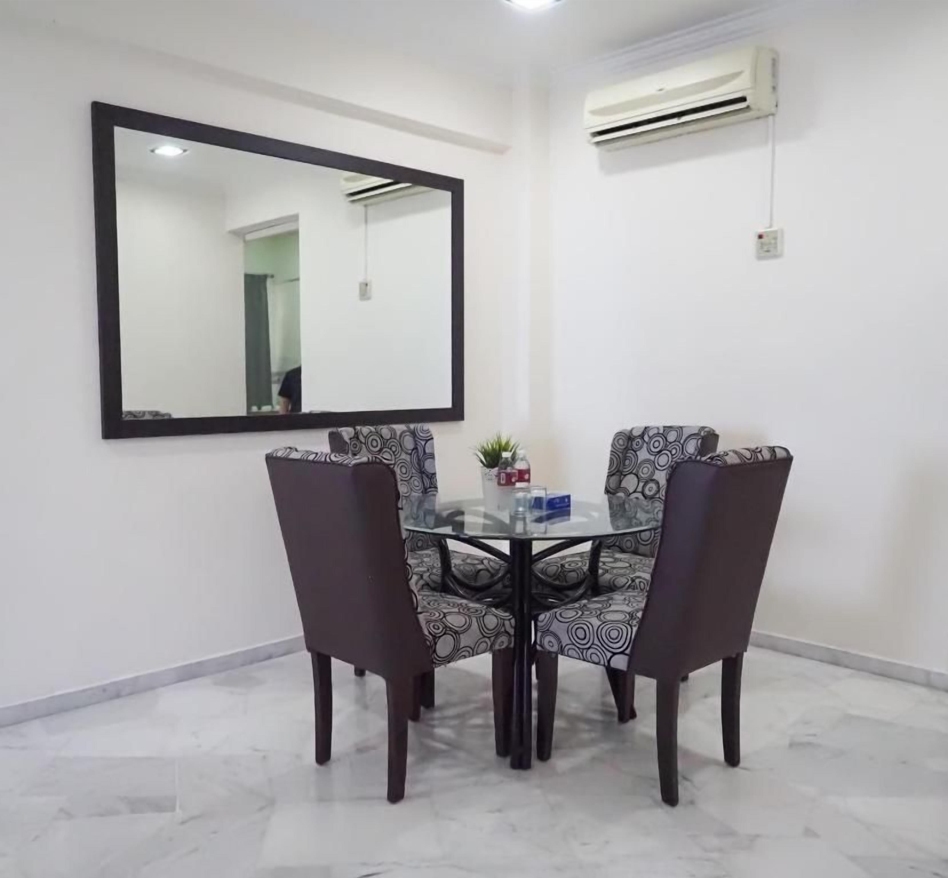 A dining area with a glass table and patterned chairs, a large mirror on the wall, and an air conditioning unit.