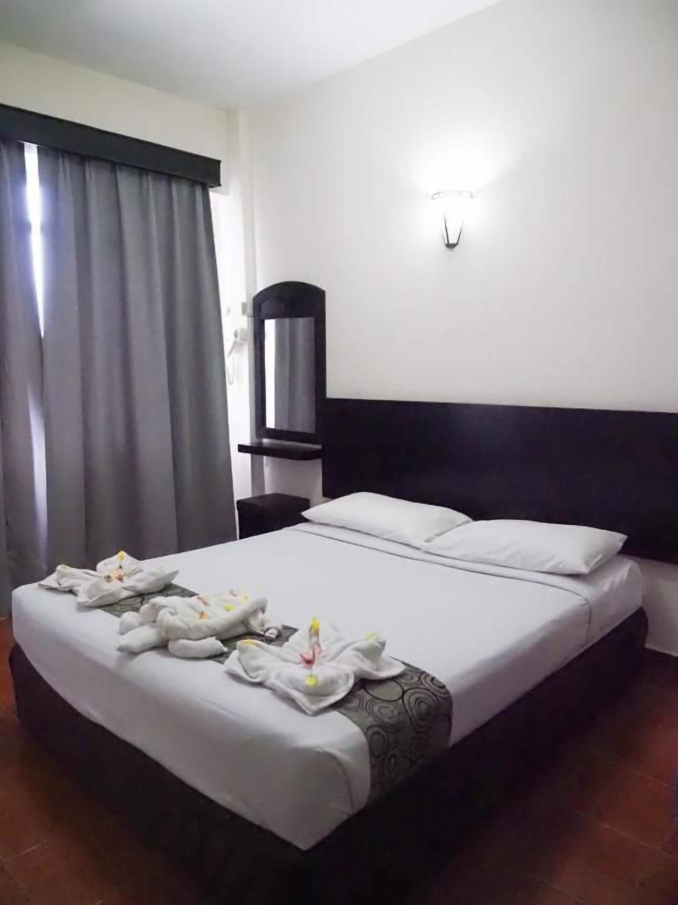 A hotel room with a bed, a nightstand, a lamp, and a window with curtains.