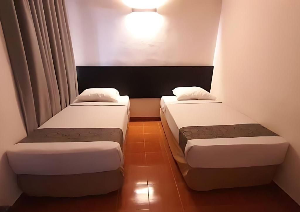 A hotel room with two single beds, a headboard, a light fixture, and a curtain.