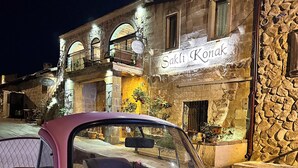 Um carro rosa estacionado em frente a um edifício com fachada de pedra e uma placa com a inscrição 'Sakli Konak'.