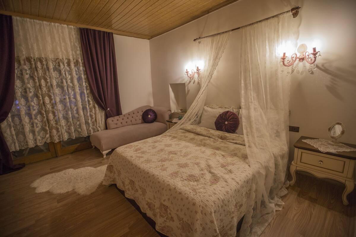 A bedroom with a canopy bed, a nightstand, a dresser, and a window with curtains.