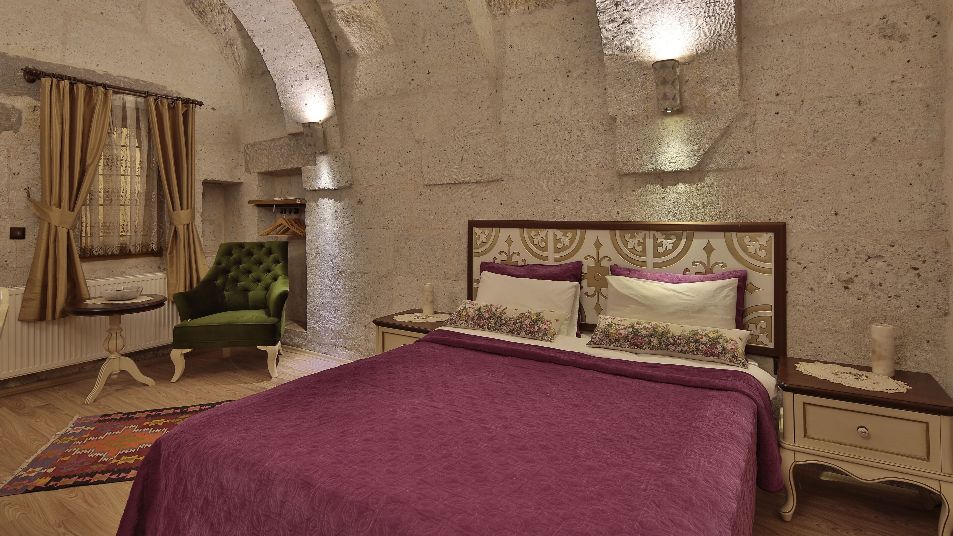 A bedroom with a bed, a green armchair, a nightstand, and a patterned rug.
