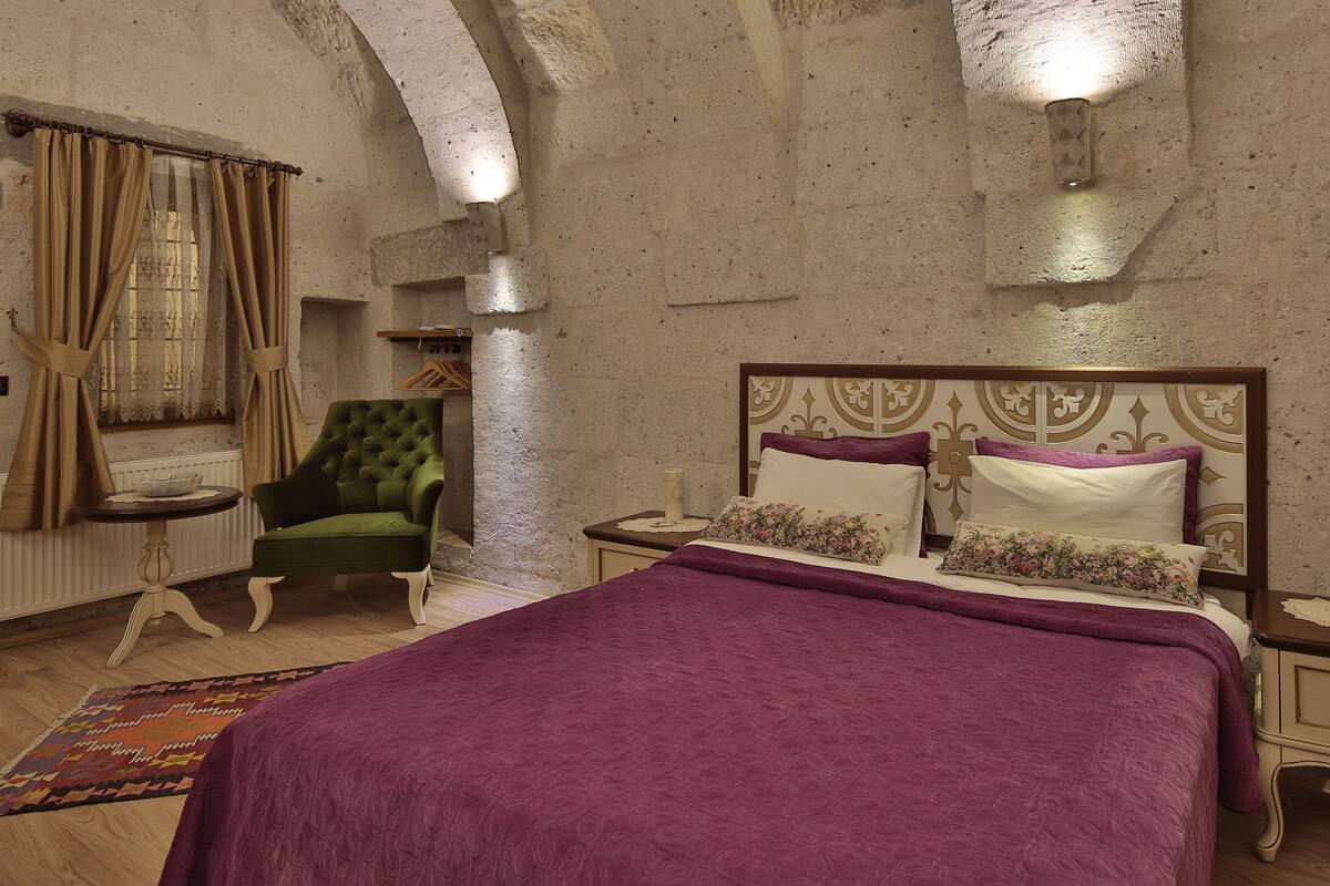 A bedroom with a bed, a green armchair, a nightstand, and a patterned rug.