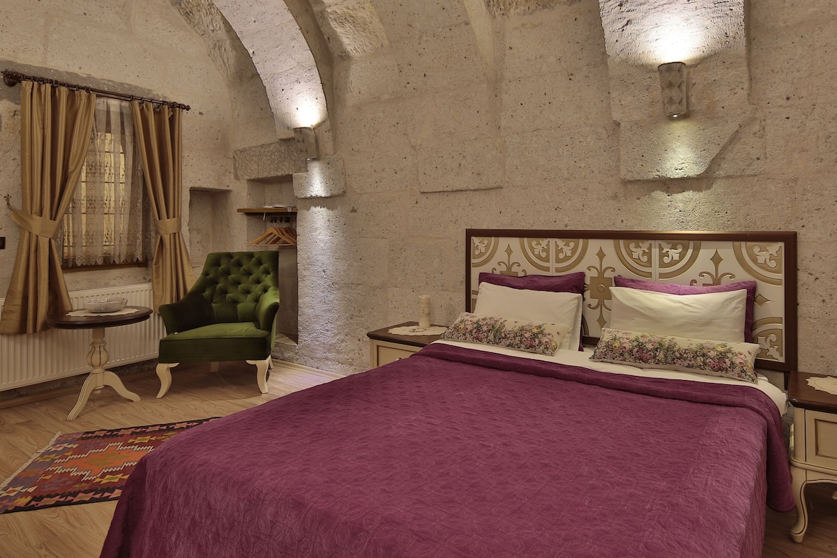 A bedroom with a bed, a green armchair, a nightstand, and a patterned rug.