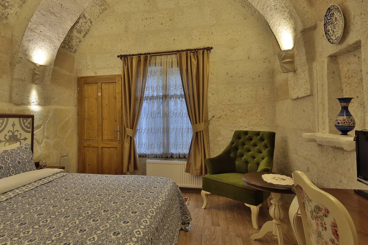 A room with a bed, a chair, a small table, and a window with curtains.