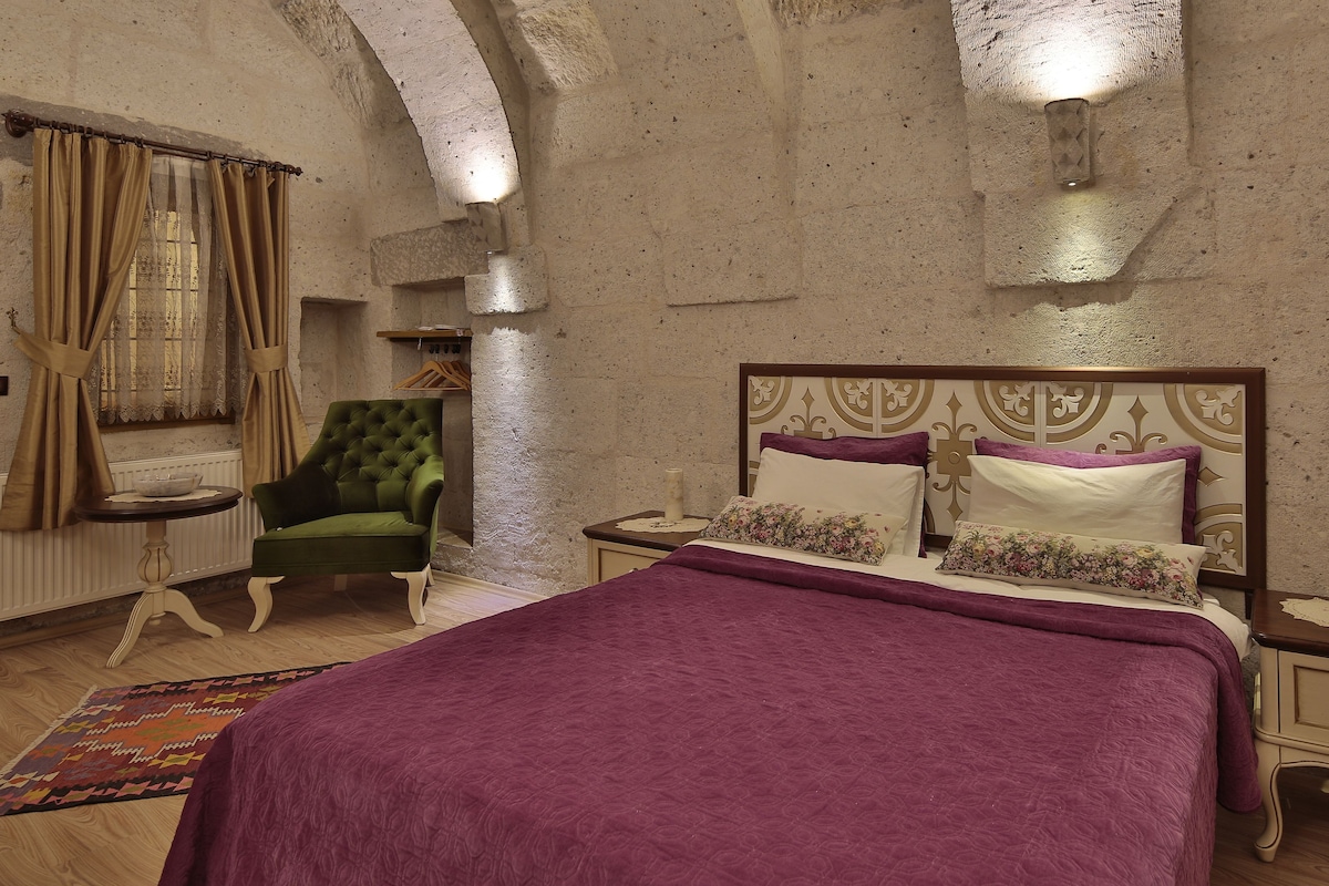 Une chambre à coucher avec un lit, un fauteuil vert, une table de chevet et un tapis à motifs.