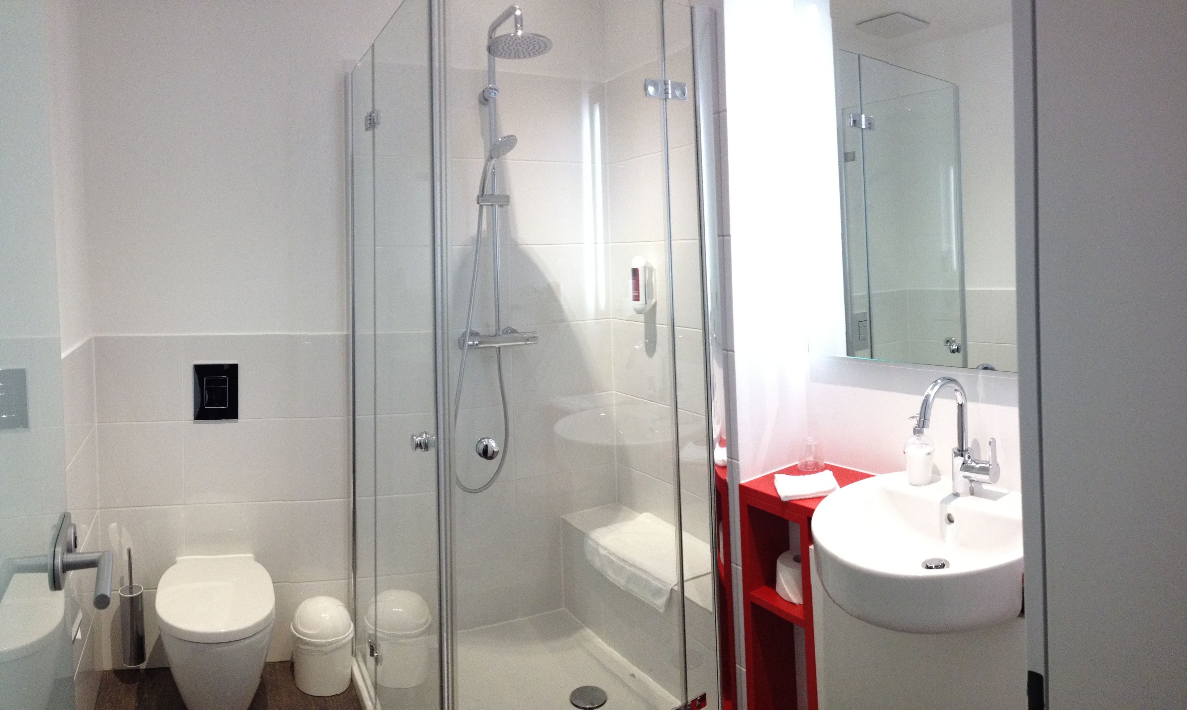 A modern bathroom with a glass-enclosed shower, a white toilet, and a red vanity with a sink.
